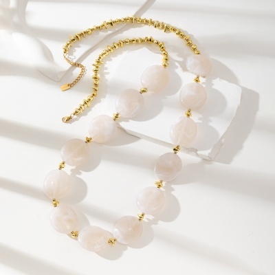 Colar com contas brancas marmoreadas e douradas em superfície branca