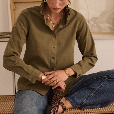 Mulher sentada com camisa verde-oliva, jeans azuis, sapatos com padrão animal print e joias douradas