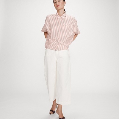 Mulher com camisa às riscas, calças largas brancas e sandálias de salto preto.