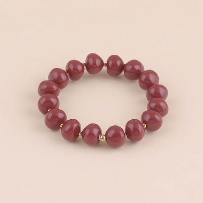 Pulseira em contas vinho e douradas sobre fundo bege claro