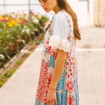 Vestido patchwork com estampas florais e bolinhas, mangas brancas bordadas num ambiente com flores