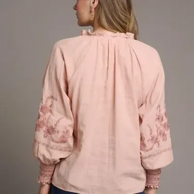 Blusa rosa clara com bordados florais nas mangas e gola com babado vista de costas