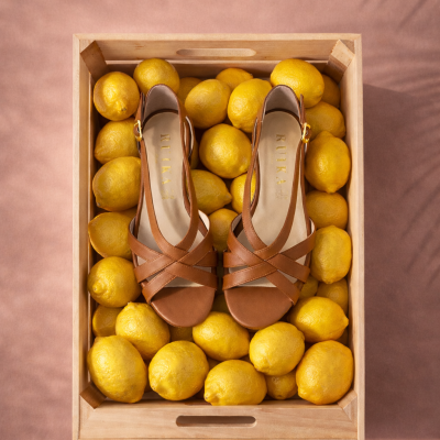 Sandálias castanhas em caixa de madeira com limões amarelos