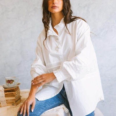 Blusa branca bordada com botões decorativos, calças de ganga azuis, livros e chávena de chá com padrão floral