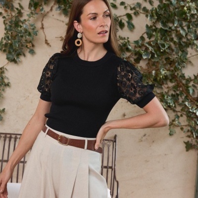Mulher com t-shirt preta de malha e mangas de renda e calças beges largas com cinto castanho