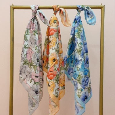 Três lenços florais de tecido pendurados num cabide dourado