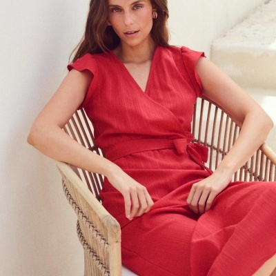 Vestido vermelho com cinto amarrado e decote em V, mulher sentada numa cadeira de madeira.