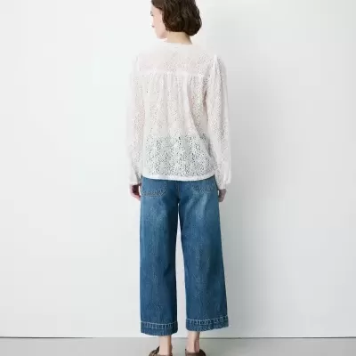 Pessoa de costas com camisa branca rendada e calças de ganga azuis largas.