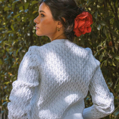 Mulher de costas com camisola branca e flor vermelha no cabelo num jardim