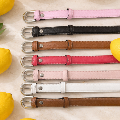 Sete cintos de pele coloridos com fivelas metálicas em fundo claro com limões amarelos