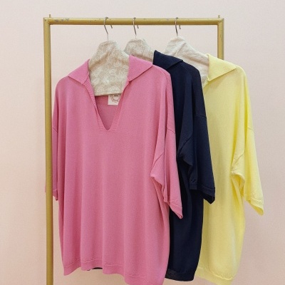 Três camisolas em rosa, azul escuro e amarelo penduradas num cabide dourado.