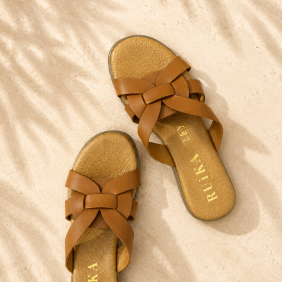 Sandálias castanhas de tiras cruzadas com marca RUÍKA na palmilha sobre piso claro com sombras de folhas