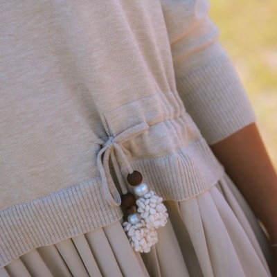 Close-up de detalhe de roupa bege com pompons e contas e saia plissada