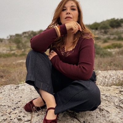 Mulher sentada com roupa vinho e preta e sapatos bordô ao ar livre