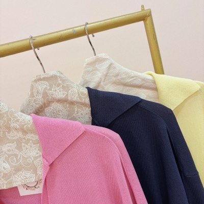 Três camisas de malha com gola em diferentes cores e padrões penduradas num suporte amarelo.