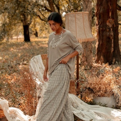 Mulher com roupa bege ao ar livre junto a cadeira de vime e candeeiro de pé