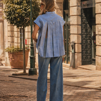 Mulher de costas com blusa azul às riscas e calças largas de ganga numa rua com edifícios antigos