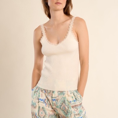 Mulher com camisola bege de alças finas e calças largas estampadas coloridas