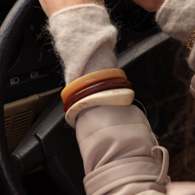 Pulseira de três braceletes em tons terra no pulso de uma pessoa ao volante de carro