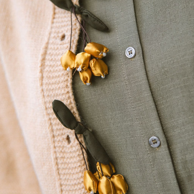 Flores decorativas amarelas em tecido penduradas numa camisola bege e camisa verde