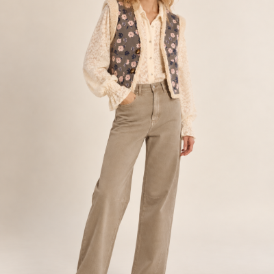 Modelo feminina com camisola creme e colete floral cinzento, calças largas bege e botas castanhas