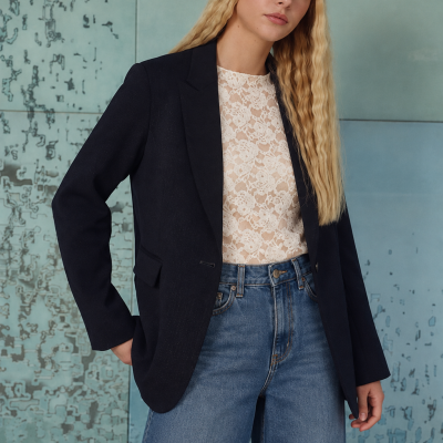 Mulher com blazer preto, blusa rendada branca e jeans azuis de corte largo