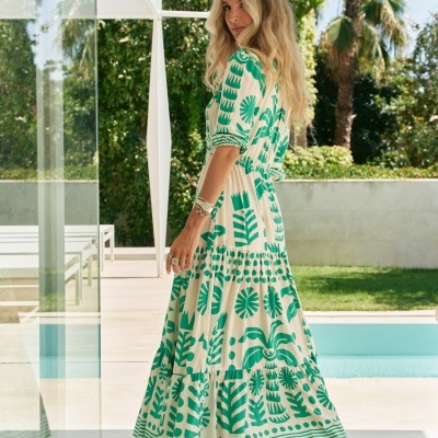 Vestido longo com padrão verde em fundo creme usado por mulher junto a uma piscina