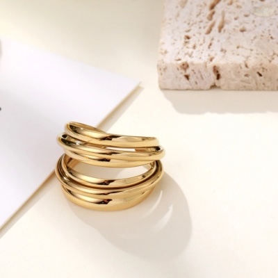 Anel dourado composto por cinco bandas lisas empilhadas sobre superfície branca
