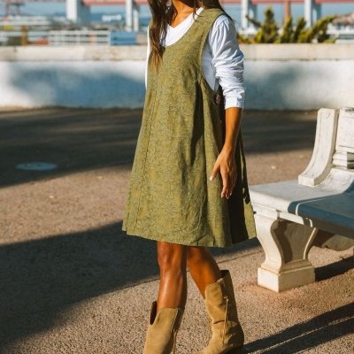 Vestido verde com padrão floral, camisola branca e botas de camurça castanhas em ambiente urbano exterior.