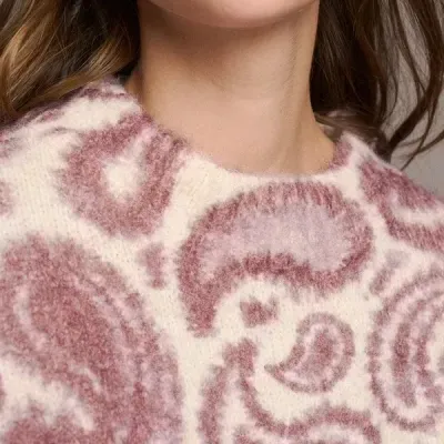 Mulher com brincos dourados e camisola de malha creme e rosa com padrão