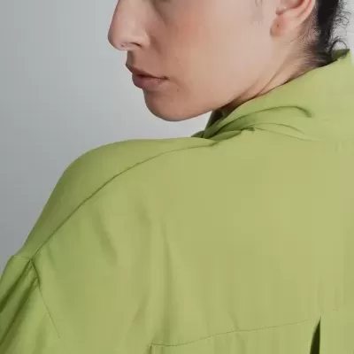 Mulher de perfil vestindo camisa verde clara com costuras e racha nas costas