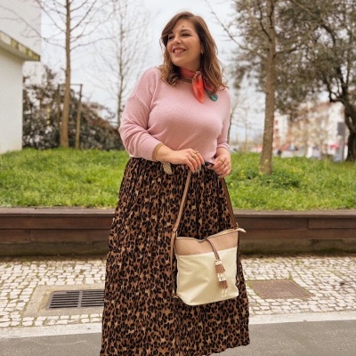 Mulher com camisola rosa, saia animal print e mala bege numa rua