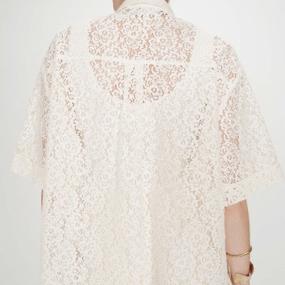 Blusa feminina de renda branca, com padrão floral e mangas curtas, vista de costas.