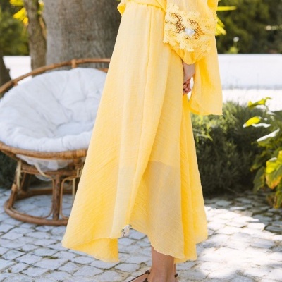 Vestido amarelo longo com renda nas mangas usado por mulher em ambiente exterior com cadeira de vime ao fundo