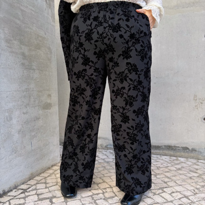 Calças pretas com padrão floral em relevo e camisa branca rendada