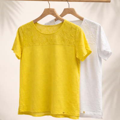 Duas t-shirts femininas, amarela e branca, com detalhes em renda, penduradas em cabides de madeira
