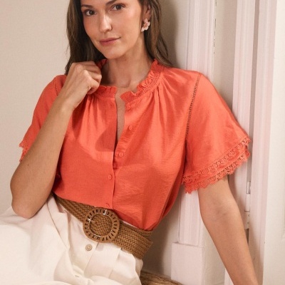 Mulher a usar blusa laranja com renda e saia creme com cinto trançado