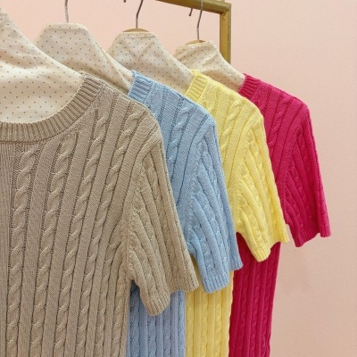 Quatro camisolas de malha coloridas com padrão de trança penduradas em cabides forrados.