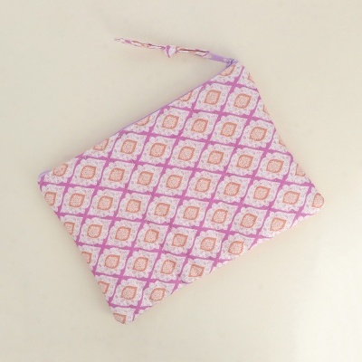 Bolsa ou estojo com padrão geométrico lilás, branco e pêssego e fecho de correr lilás.