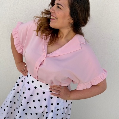 Mulher com blusa rosa de manga curta com folhos e saia branca com bolinhas pretas