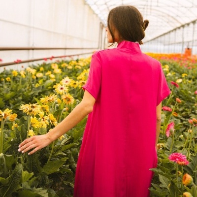 Mulher de costas num vestido fúcsia numa estufa com flores amarelas e cor-de-rosa