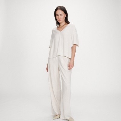 Mulher com conjunto de top e calças largas bege claro e colar dourado.