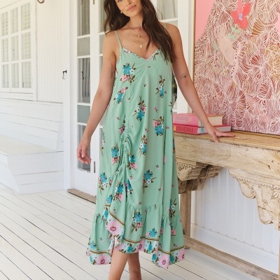 Vestido longo verde água com padrão floral usado por mulher em ambiente branco e decoração com mesa antiga de madeira.