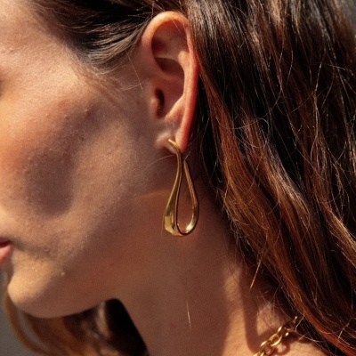 Brinco dourado em forma de gota e corrente dourada usados por mulher