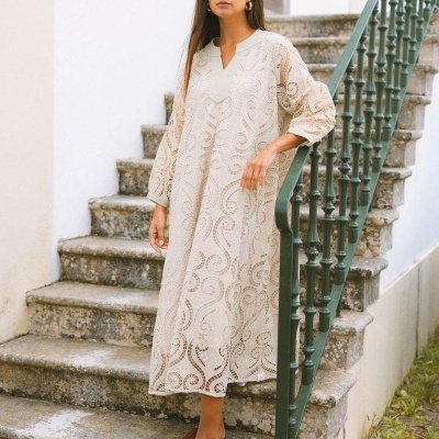 Vestido comprido de renda creme com padrão arabescos em escadaria exterior.