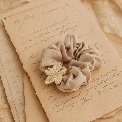 Elástico de cabelo bege com flor dourada sobre papel envelhecido