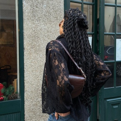 Pessoa de costas com blusa preta de renda e bolsa castanha ao ombro