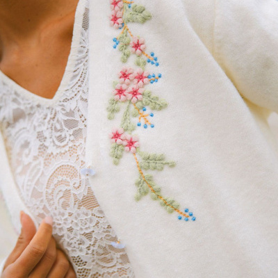 Casaco branco de lã com bordado floral colorido e blusa branca de renda.