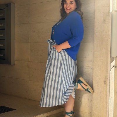 Mulher com blusa azul, saia aos riscos e alpercatas azuis nas escadas de pedra