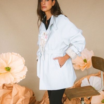 Mulher com casaco branco, flores cor de pêssego e cadeira de madeira ao fundo